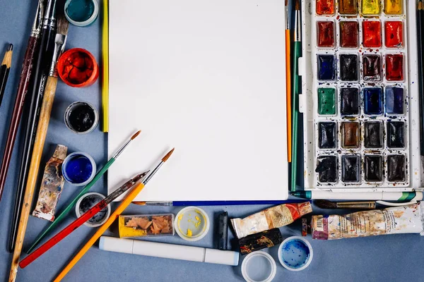 Em uma mesa azul são suprimentos artísticos, papel, escovas e aquarelas, lápis — Fotografia de Stock