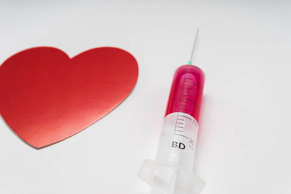 on a white surface is a medical syringe and a drawing of a red heart