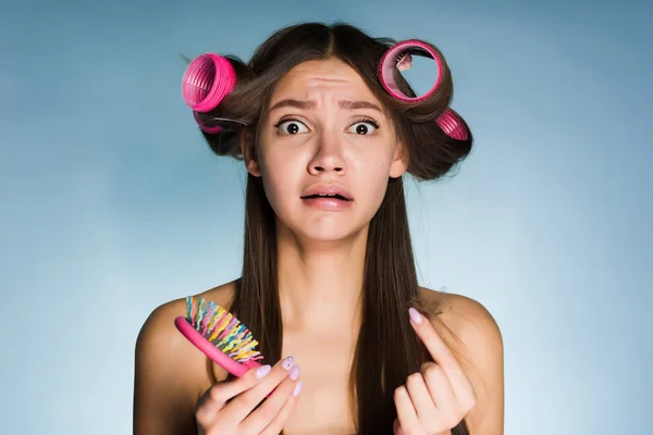 Insatisfaisant une jeune fille n'a pas le temps de se préparer pour une fête, faire une coiffure, sur sa tête un gros bigoudi rose, garde un peigne — Photo