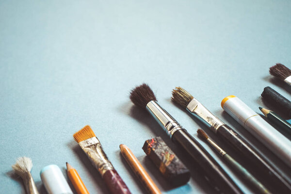 на синем фоне есть много кистей разных размеров, карандаши и маркеры
