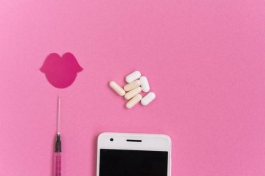 pembe bir arka plan üzerinde beyaz bir akıllı telefon, bir şırınga, tabletler ve kırmızı dudaklar bir çizim olduğunu