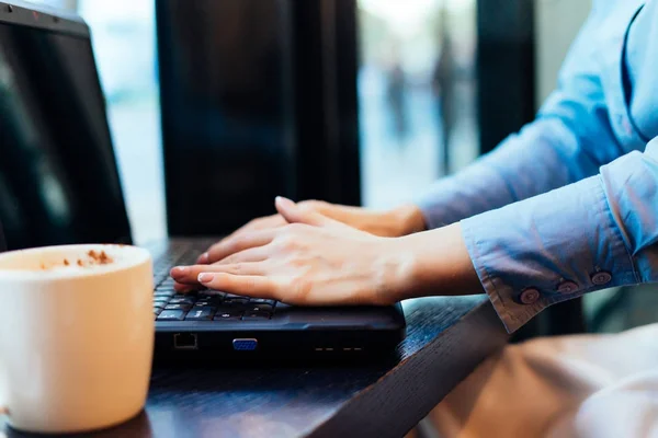 香り豊かなコーヒーのカップの隣に、カフェでノート パソコンのために働く女の子フリーランサー — ストック写真