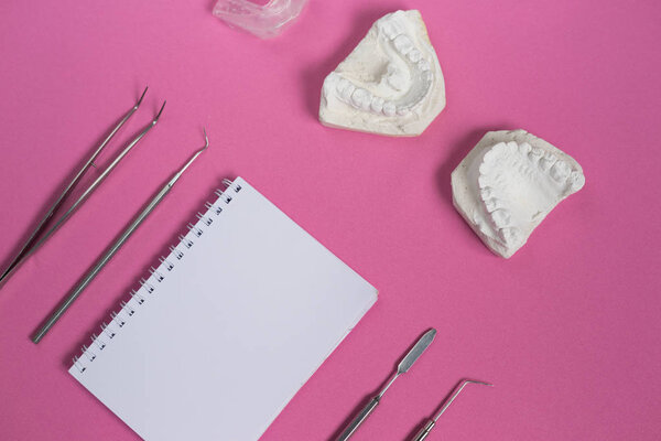 на поверхности мемориальной доски лежат гипсовый слепок зубов, зубных инструментов и ноутбука
