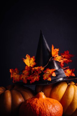 siyah bir arka plan üzerinde turuncu Halloween pumpkins, büyük bir siyah cadı şapka ve akçaağaç yaprakları vardır.