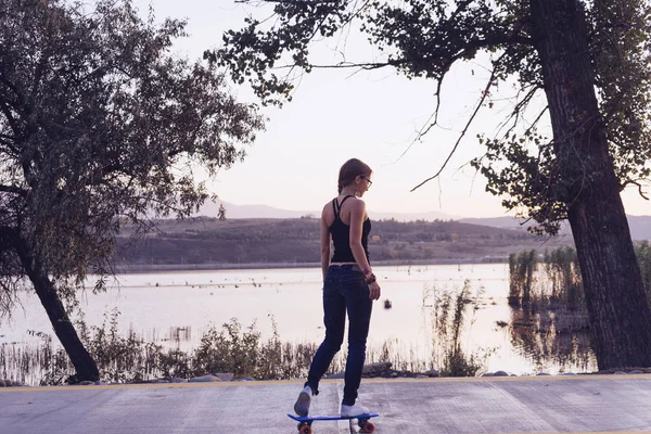 Stijlvolle jong meisje schaatsen op een achtergrond van de rivier — Stockfoto