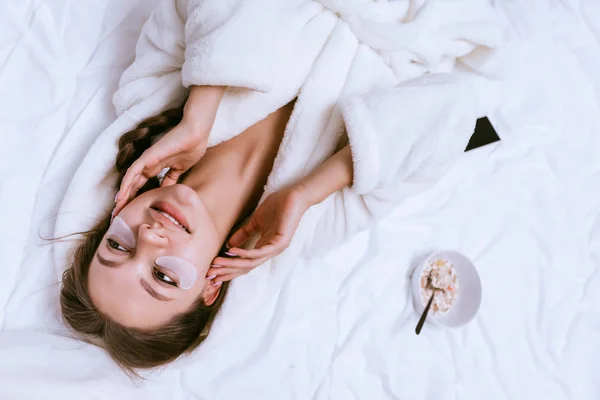 Menina feliz acordou cedo, deitado na cama, próximo café da manhã de mingau de aveia, sorrindo — Fotografia de Stock