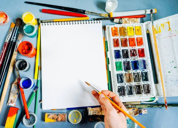 On the blue surface are artistic supplies, paper, watercolors and gouache, brushes and pencils — Stock Photo, Image