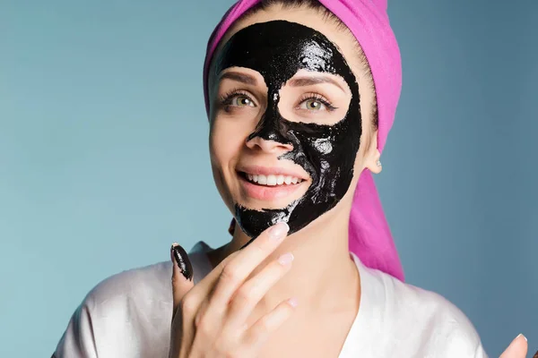 Felice ragazza si prende cura del suo viso, mette una maschera nera sul suo viso — Foto Stock