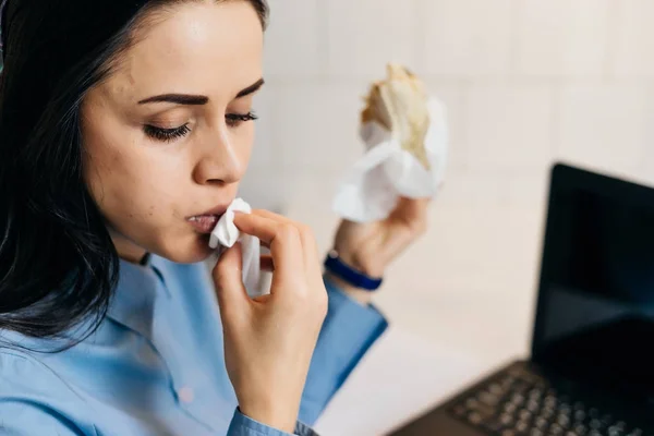 Busy young girl freelancer eating breakfast in a cafe, working on a laptop — Stock Photo, Image