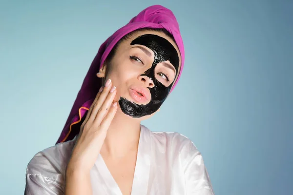 Une jeune fille drôle prend soin d'elle-même, met un masque nettoyant noir sur son visage — Photo