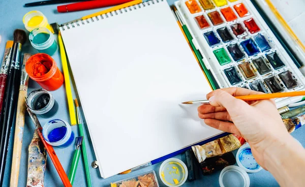 On a blue table are artistic supplies, paper, watercolors and gouache, many brushes — Stock Photo, Image