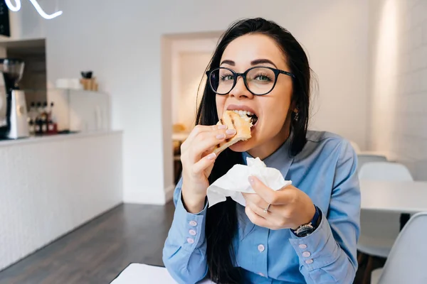 カフェでサンドイッチを食べる眼鏡と青シャツの面白い女性実業家 — ストック写真