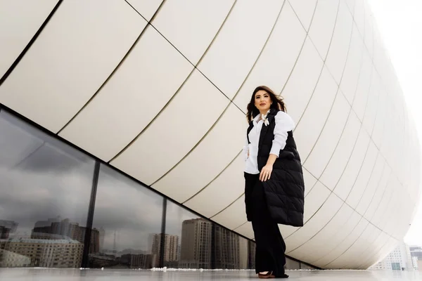 Stylish young girl in a black suit posing near an unusual building in Baku — Stock Photo, Image