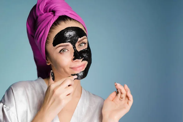Una giovane ragazza attraente si prende cura del suo viso, una maschera detergente nera — Foto Stock