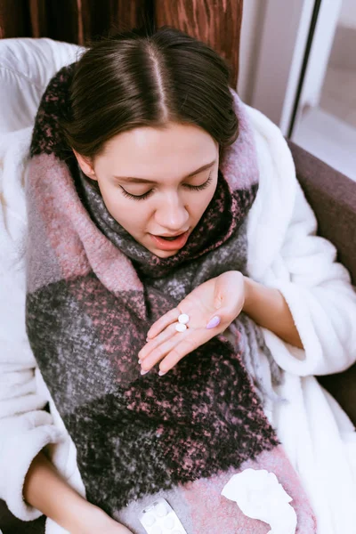 Mladá dívka onemocněla kvůli chladné zimní počasí, její krk bolí, je držitelkou pilulku v ruce — Stock fotografie