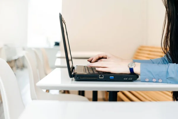 Freelancer menina em uma camisa azul trabalha em um café para um laptop — Fotografia de Stock