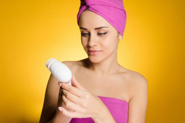 Kafasındaki bir pembe havlu ile genç kız elektrikli bir fırça ile yüzünde cildi temizler