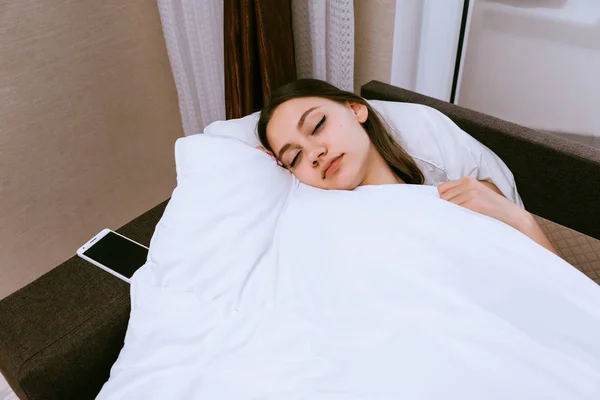 Молодая девушка спит под одеялом, у нее выходной, она не слышит будильник — стоковое фото