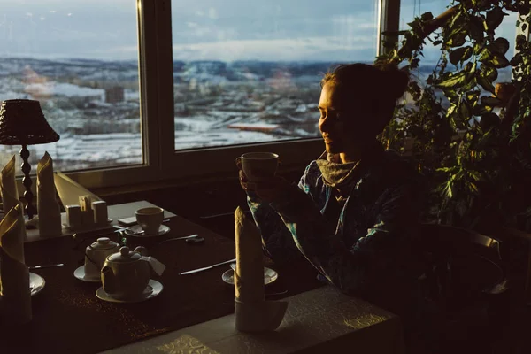 Ragazza seduta in un caffè a un tavolo, al sole, fuori dalla finestra bianco inverno — Foto Stock