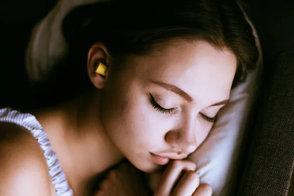 Молода дівчина спить, у вухах жовті вушні пробки проти шуму — стокове фото