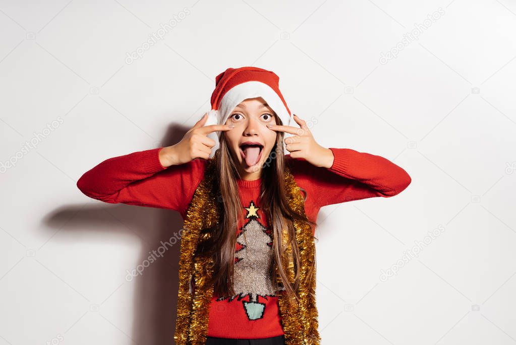 funny young girl shows her tongue, in a red cap like Santa Claus, waiting for the new year