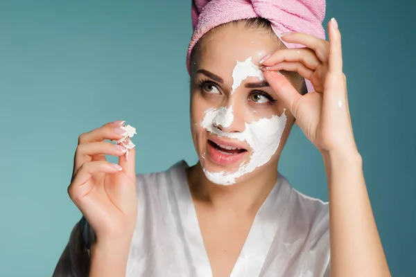 Beautiful young girl with a pink towel on her head applies a white cleansing mask on her face — Stock Photo, Image