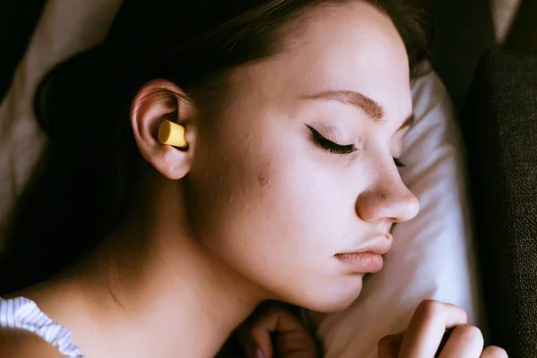 Menina dormindo na cama, nos ouvidos tampões de ouvido amarelos contra o ruído — Fotografia de Stock