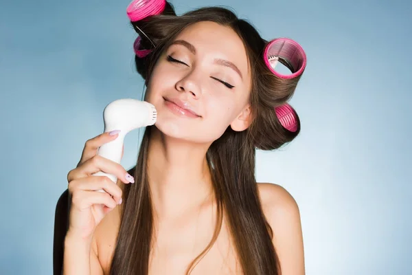 Ευτυχής όμορφη κοπέλα καθαρίζει το δέρμα στο πρόσωπό της με μια ηλεκτρική βούρτσα, σχετικά με το κεφάλι σίδερα — Φωτογραφία Αρχείου