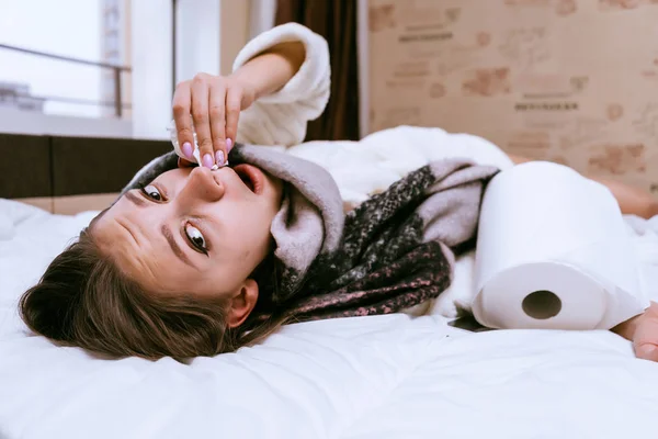 Verdrietig meisje ligt op bed, op haar hals een warme sjaal, ziek van het koude winterweer — Stockfoto