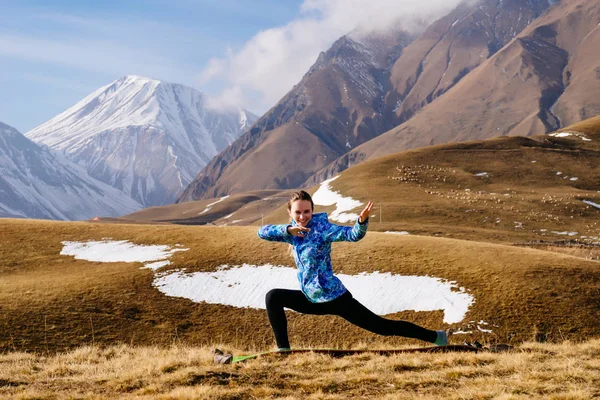 Девушка в синей куртке занимается йогой на фоне Кавказских гор, любит путешествовать — стоковое фото