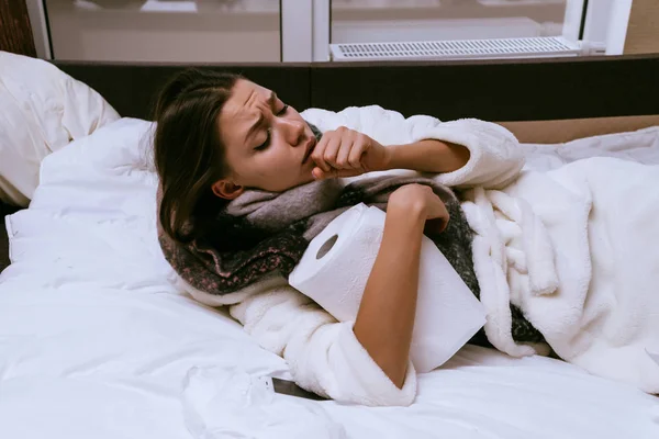 Η νεαρή κοπέλα είναι πολύ άρρωστος εξαιτίας the κρύος χειμώναs καιρόs, πονάει το λαιμό, βήχα, έγκειται στο κρεβάτι — Φωτογραφία Αρχείου