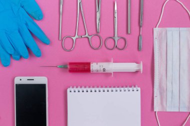 pembe bir yüzeye yalan tıp aletleri, mavi eldiven, bir akıllı telefon, bir not defteri
