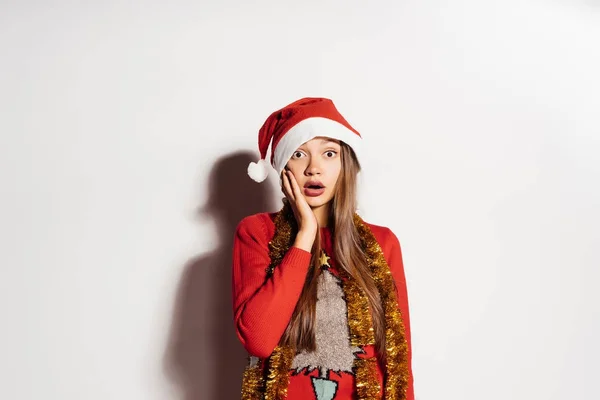 Triste joven sorprendida en ropa de Navidad y una gorra esperando un nuevo año y Navidad —  Fotos de Stock