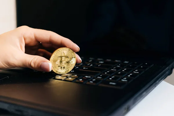 Chica financiera que trabaja en un ordenador portátil, sosteniendo en su mano un valioso bitcoin de oro — Foto de Stock