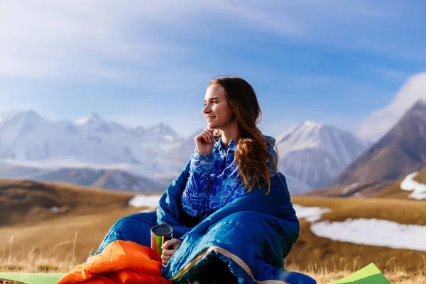 Mavi bir ceket ve etkin kız güneş ve temiz dağ havası, bir uyku tulumu içinde oturan zevk devreye girer — Stok fotoğraf