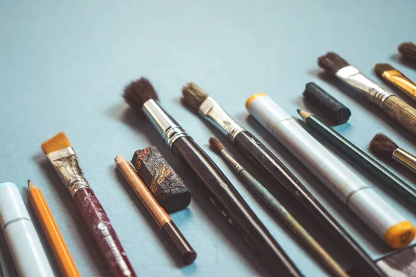 På en blå bakgrund finns det konstnärliga penslar i olika storlekar, pennor och markörer — Stockfoto