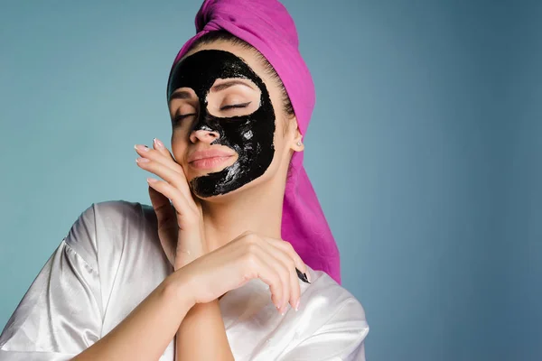 Belle jeune fille avec une serviette rose sur la tête, souriante, veut être belle, sur son visage un masque nettoyant noir — Photo