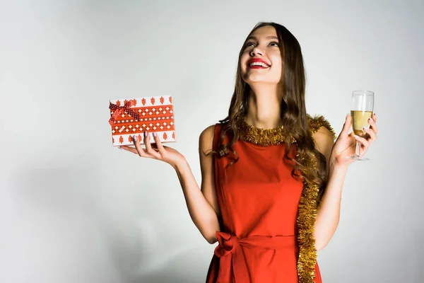 Счастливая смеющаяся девушка в красном платье празднует новый 2018 год, получила подарок от Санта Клауса, держит в руке бокал шампанского — стоковое фото