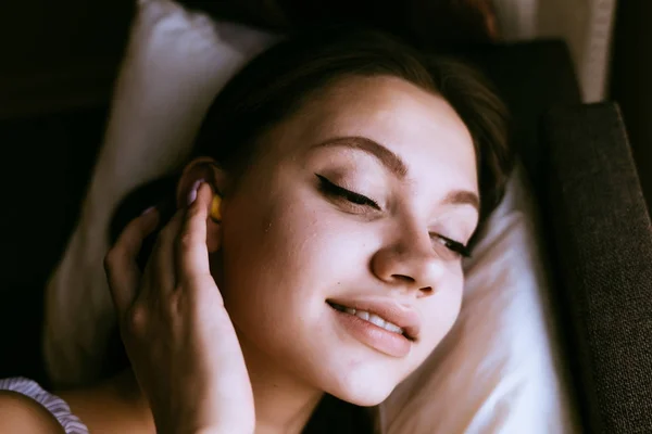 Lächelndes junges Mädchen ging zu Bett, in den Ohren gelbe Ohrstöpsel gegen Straßenlärm — Stockfoto
