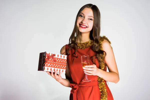 Happy laughing girl in a red dress received a gift for the new year, holding a glass of champagne — Stock Photo, Image