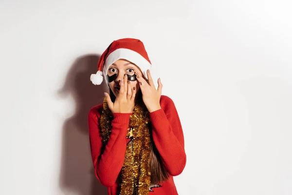 Menina surpresa na roupa festiva de Ano Novo cola manchas pretas de silicone sob os olhos — Fotografia de Stock