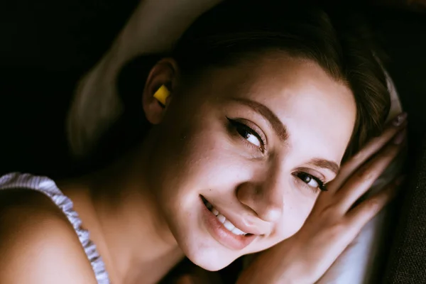 Szczęśliwa młoda dziewczyna uśmiechając się, chce się spać, w uszy żółte zatyczki do uszu przeciw hałas z ulicy — Zdjęcie stockowe