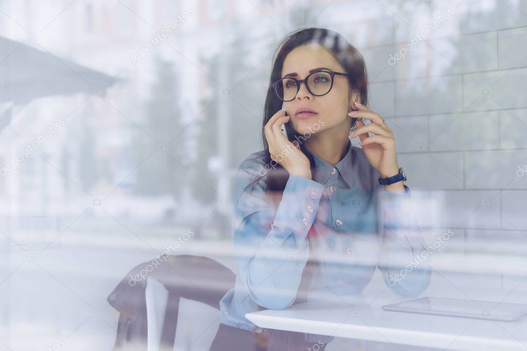 pensive young girl freelancer with glasses talking on the phone about business