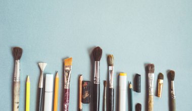 mavi bir yüzeye sanatsal fırçaların farklı boyutlarda, kurşun kalem ve tükenmez kalem vardır