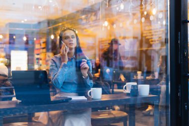 bir kafede bir dizüstü bilgisayarda akşam çalışma, telefonda konuşurken ve bir şey hakkında düşünme genç esmer kız serbest meslek