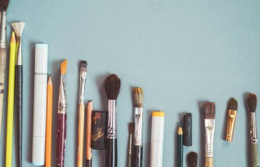 mavi bir yüzeye sanatsal fırçaların farklı boyutlarda, kurşun kalem ve tükenmez kalem vardır