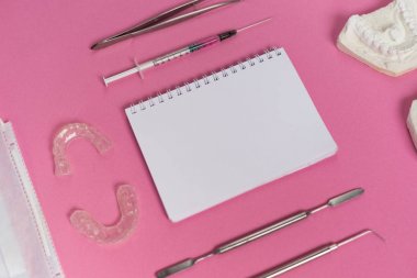 pembe bir yüzey üzerinde beyaz bir defter, diş aletleri ve alçı diş yalan