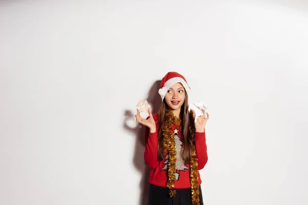 Happy νεαρό κορίτσι σε ένα κόκκινο πουλόβερ Χριστουγέννων κρατώντας ένα χριστουγεννιάτικο δέντρο παιχνίδια, γύρο λαιμό χρυσό πούλιες — Φωτογραφία Αρχείου