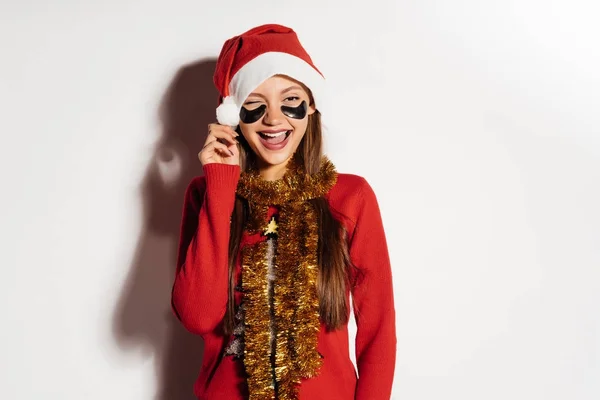 Γελώντας νεαρό κορίτσι με τα κόκκινα ρούχα είναι ευχαριστημένοι με το νέο έτος 2018, κάτω από τα μάτια μπαλώματα μαύρο σιλικόνης — Φωτογραφία Αρχείου