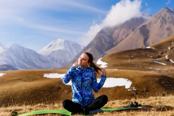 Junges sportliches Mädchen in blauer Jacke meditiert vor dem Hintergrund der Kaukasusberge, entspannt — Stockfoto